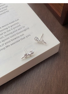 Macro detail of silver bow earrings with textured finish on a vintage book page