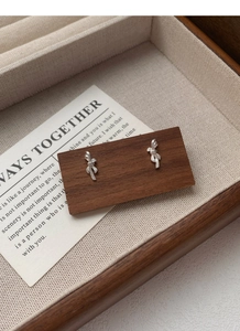 Detail of S999 sterling silver bow knot earrings with a brushed metal texture on wood