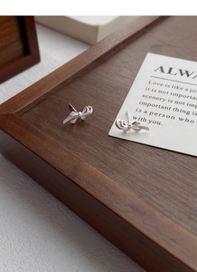 Detailed view of silver bow earrings with fine brushed texture on a wooden tray