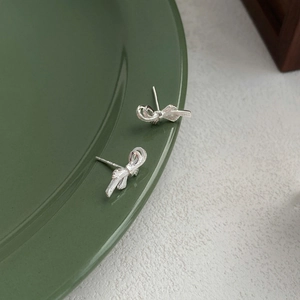 Elegant S999 sterling silver bow knot stud earrings displayed on a dark green ceramic tray