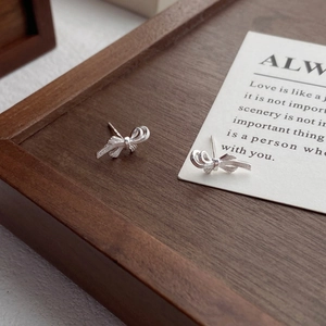 Minimalist S999 sterling silver bow knot earrings with brushed texture on wooden tray