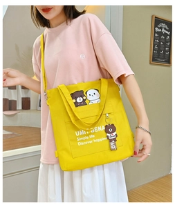 Detail of yellow canvas tote bag featuring panda graphics and cute bear pendant charm
