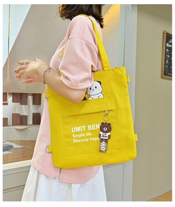 Detail of yellow canvas tote bag with cartoon bear pendant and large front pocket