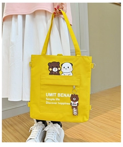 Detail of yellow canvas tote bag featuring cartoon bear print and bear charm accessory