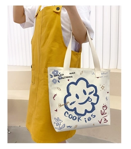 Detail view of a white canvas tote bag with blue cartoon clouds and artistic graffiti