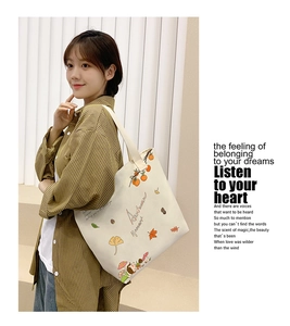 Close-up of beige canvas tote bag with autumn harvest illustrations and shoulder strap