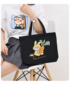 Detail of black canvas tote bag featuring a cute yellow cartoon rabbit and art text