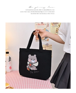 Close-up of a stylish black canvas handbag with a cute brown bear graphic and twin handles