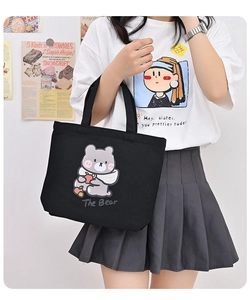 Detail shot of a black canvas tote bag featuring a cute grey bear graphic and text