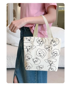 Artistic portrait line drawing on cream canvas tote bag held by model in casual setting