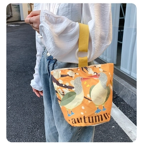 Detail view of the orange canvas bucket bag showing autumn bird prints and yellow handles