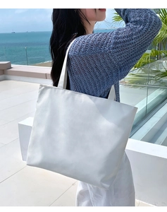 Detail view of a large white canvas tote bag worn by a model on a sunny beach terrace