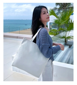 Close-up of minimalist large white canvas tote bag worn by a model in a coastal setting