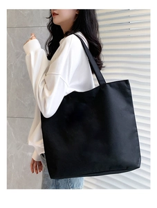 Minimalist black canvas tote bag shown worn on the shoulder to illustrate size and fit
