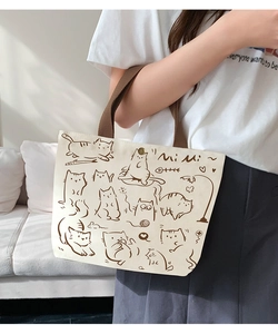 Detail of canvas tote bag with cartoon cat prints, metal snap button, and fabric shoulder strap