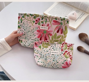 Detail of pink floral embroidered canvas cosmetic bags held by a model in a lifestyle scene