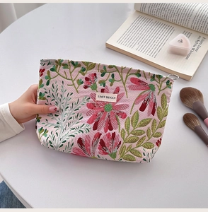 Close-up of pink canvas cosmetic bag with floral embroidery and brand label on a desk