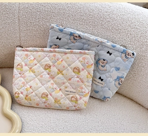 Detail of quilted cosmetic bags featuring cute cartoon patterns on textured white sofa