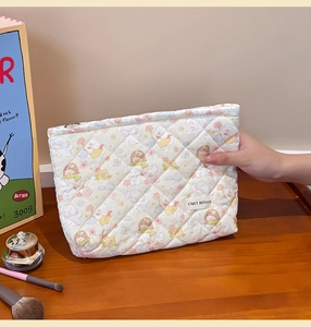 Detail of quilted cotton cosmetic bag featuring cute cartoon print and woven brand label