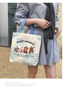 Outdoor shot of a cream Capybara canvas tote bag with blue handles and cartoon print