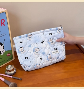 Close-up of quilted blue makeup bag with cute dog prints held by a hand in a daily scene