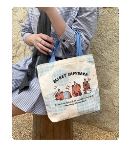 Detail of cream canvas tote bag with cute cartoon capybara prints and blue straps
