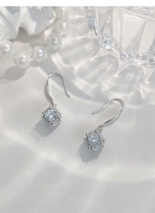 Macro shot of S925 silver cube earrings with a sparkling zircon center on a water-ripple background