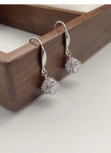 Macro shot of silver geometric earrings with sparkling cubic zirconia on a wood tray