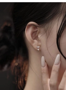 Detail of S999 sterling silver bow stud earring with small round bead on model ear