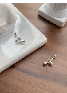 Detail of silver bow stud earrings with screw ball back on a textured wooden surface