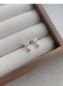 Detail of silver bow earrings with shiny ball drop displayed on a linen jewelry box