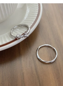Close-up of S925 sterling silver bow and twisted wave rings on a ceramic edge