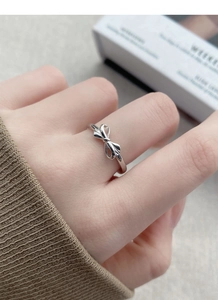 Detail shot of a silver bow knot ring worn on index finger with a minimalist style
