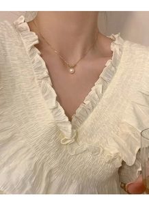 Pendentif perle élégant sur une chaîne dorée délicate porté sur un haut à volants crème
