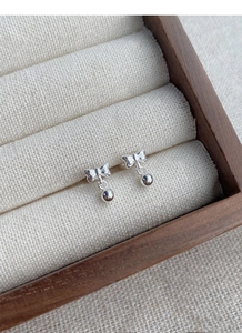 Detailed close-up of S999 sterling silver bow earrings with round beads on wood display