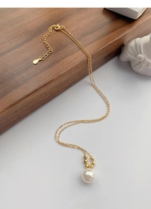 Détail d'un collier en argent S925 doré avec pendentif perle sur support en bois