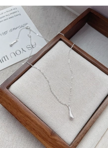 Macro shot of S925 sterling silver frosted waterdrop pendant on a wooden frame