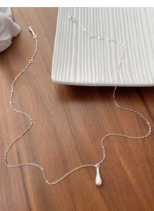 Close-up of brushed silver water drop pendant on a delicate chain on a wooden surface