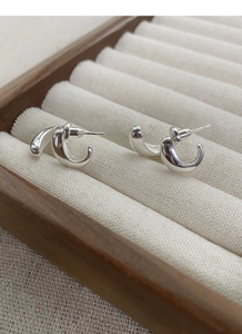 Macro detail of S925 sterling silver C-shape earrings on a beige velvet jewelry box