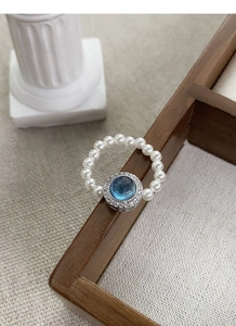 Detailed macro of beaded ring with blue gemstone and pearl band on wooden tray