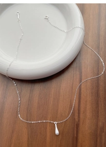 Macro detail of the silver brushed matte water drop pendant on a delicate chain necklace