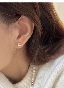 Macro shot of silver croissant-shaped stud earring worn on ear with knit background