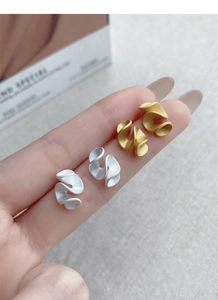 Macro view of gold and silver S925 sterling silver pleated ribbon stud earrings in hand