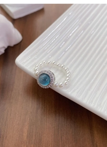 Macro shot of silver ring with blue gemstone, diamond halo and pearl elastic band