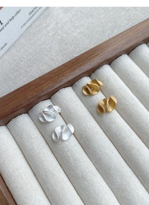 Macro detail of matte gold and silver ruffled stud earrings on velvet jewelry display