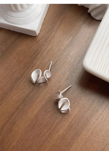 Macro detail of matte S925 sterling silver ruffled earrings on a ceramic dish