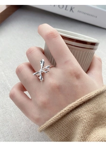 Detail of silver S925 bow ring worn on finger with a minimalist lifestyle background