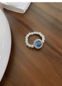 Detail of beaded pearl ring featuring a blue cat-eye stone and zircon halo setting
