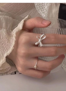 Macro detail of S925 silver bow ring and pearl band worn on hand holding glass