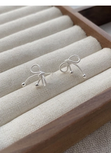 Macro shot of silver bow stud earrings with twisted rope texture and bead details
